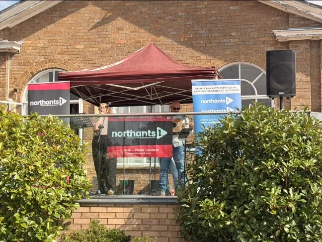 Two performers with northants 1 poster in front of them